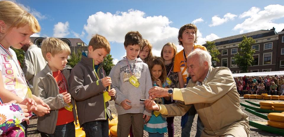Kinderen krijgen uitleg van een man over de kaasmarkt in Alkmaar